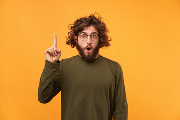 Great idea. Handsome man keeping finger raised and looking at camera while standing against yellow...