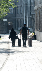 Back turned couple, a man and a veiled woman, walking with trolley luggages