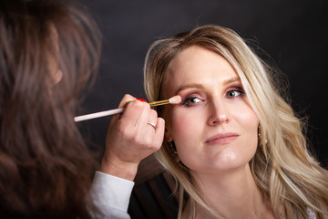 Blonde junge Frau wird von Visagistin mit Pinsel geschminkt 