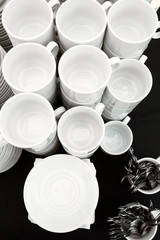 A table set of white mugs, plates and spoons on a buffet