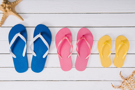 top view of yellow, blue and pink flip flops on white wooden background