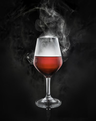 Red wine in glass with smoke on black background
