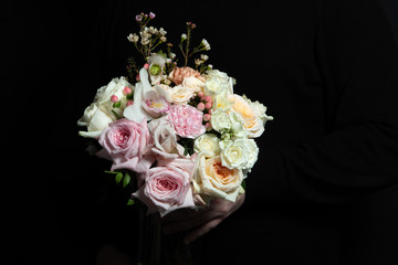 Very delicate handmade bouquet in the hands of the florist, a great gift, fresh and neat, bridal bouquet on a black background
