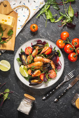 Fresh seafood salad, mussels, shrimp, fresh vegetables and herbs on black stone background