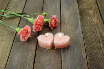 pink carnations, and heart-shaped candles on a wooden background