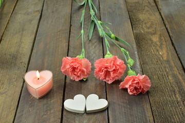 pink carnations, hearts and candle on a wooden background