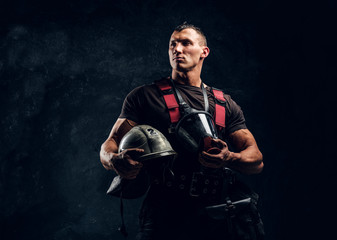 Portrait of a handsome muscular fireman holding a helmet and oxygen mask standing in the studio...