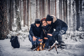 Fototapeta na wymiar A group of hiker friends went on a hike in the snowy forest, warming sitting by the fire