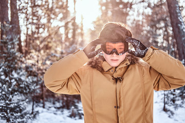 Portrait of a young snowboarder dressed in warm clothes and protective goggles standing in a snowy...