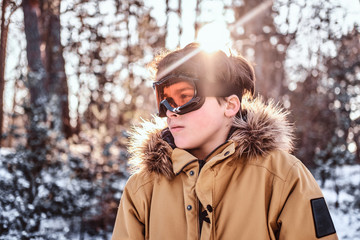 Portrait of a young snowboarder dressed in warm clothes and protective goggles standing in a snowy...