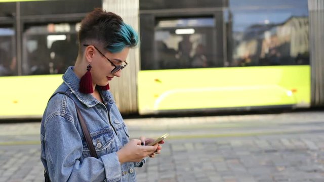 beautiful hipster caucasian girl with a smartphone in hand in jeans jacket turns to the left the camera moves to the right