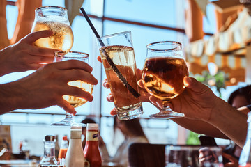 Group of friends enjoying a beer in outdoors cafe, clinking with glasses of beer against the clear...