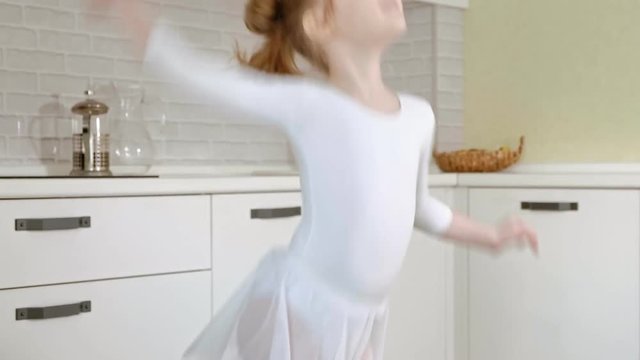 A happy little girl in a white gymnastic swimsuit trains, dances with a ribbon for rhythmic gymnastics, jumps and performing professional exercises.