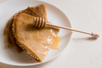 traditional Russian pancakes with honey on a light background.carnival.copy spase.pancake week.pancakes with honey syrup on a white plate 