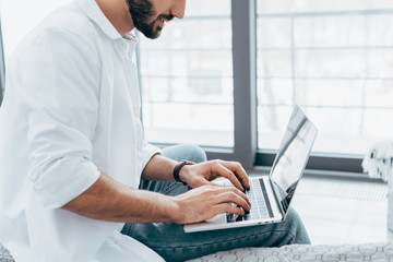 Partial view of man in white shirt and jeans typing on laptop keyboard