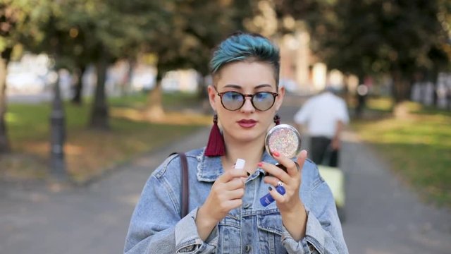 beautiful girl with punk hairstyle, jeans jacket, with glasses, paints lips, slow motion