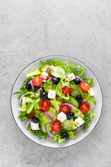 Fototapeta na wymiar Vegetable salad with fresh cucumber, tomato, olive, onion, lettuce and feta cheese. Healthy food. Top view