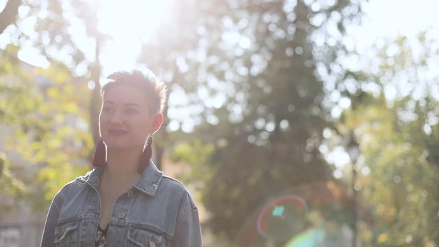 beautiful caucasian girl with punk hairstyle, stands, jeans jacket, sunlight, slow motion