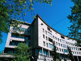 Bottom view of the constructivist building of the 1930s, surrounded by green trees on a Sunny day....