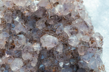 Amethyst natural crystal cluster with Goethite inclusions from Brazil on white snow at a sunny winter day.