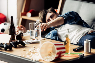 selective focus of man taking glass of water on coffee table while lying on sofa
