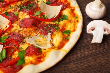 Mushrooms and Italian pizza with parmezan cheese, tomatoes, salami, pepperoni and green basil on a brown table