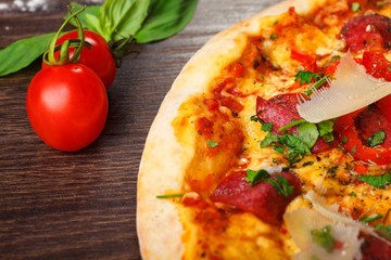 Pizza Italian with parmesan cheese, tomatoes, salami, pepperoni and green basil on a brown table decorated by mushrooms, red sweet pepper and cherry tomatoes. Top view.