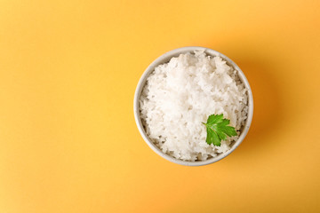 Bowl of boiled rice on color background, top view with space for text