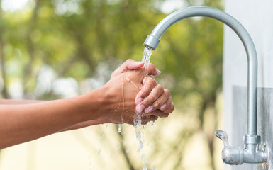 Man washing hand after working with outdoor faucet sink, cleaning hygiene protection concept with flowing water and green forest background