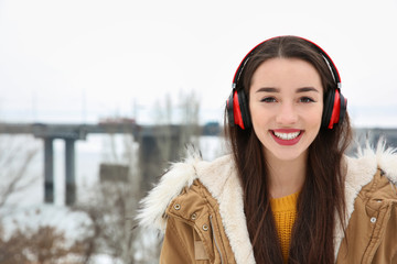 Beautiful young woman listening to music with headphones outdoors. Space for text