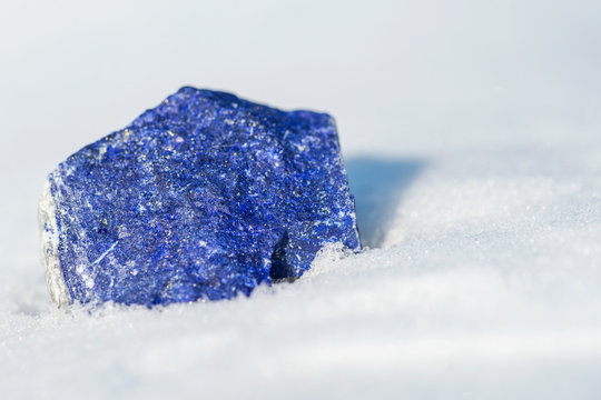 Top Grade Rough Rich Blue Lapis Lazuli with golden pyrite and white calcite inclusions from Afghanistan on white snow at a sunny winter day.