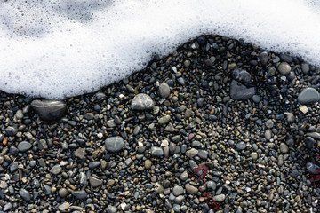 Sea foam washing over pebbles at a beach