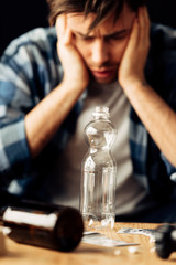 selective focus of empty bottle with man suffering from hangover on background
