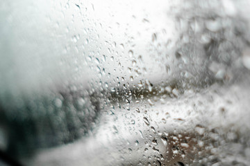 View through water drops on a weeping car window on background in winter season