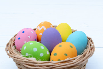 Happy Easter Day. Easter eggs concept. Closeup Colorful Easter eggs in nest and basket on white wooden background.