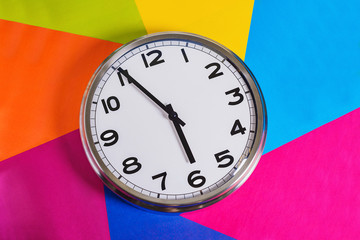 Steel clock on a multicolored background, the hands indicate five minutes to six. Close up. The...