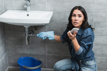 Worried girl repairing pipe with wrench and talking on smartphone
