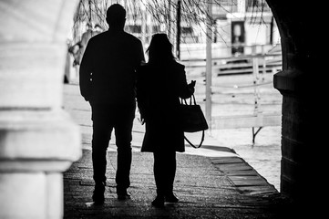 Silhouettes of couple walking under bridge in border river