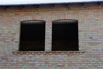 two empty black windows on a brown brick wall of an unfinished house