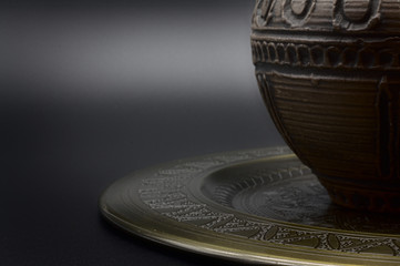 Antique greek vase on golden plate on black slate table, dark background with slight shadow on the plate