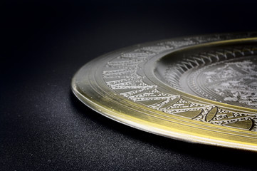 Antique golden plate on black slate table, dark background with slight shadow on plate