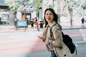 Fototapeta premium travel female backpacker holding cellphone searching route on line map app cheerfully walking on road. beautiful woman tourist using smart phone carrying bag happy sightseeing city san francisco.