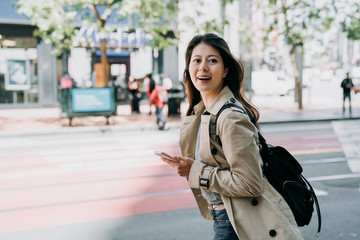 travel female backpacker holding cellphone searching route on line map app cheerfully walking on road. beautiful woman tourist using smart phone carrying bag happy sightseeing city san francisco.