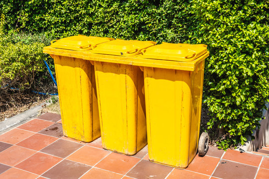 Row of yellow plastic trash bin for wate separation and recycling on green leaf background