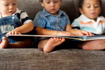 Three little boys reading a book on a sofa