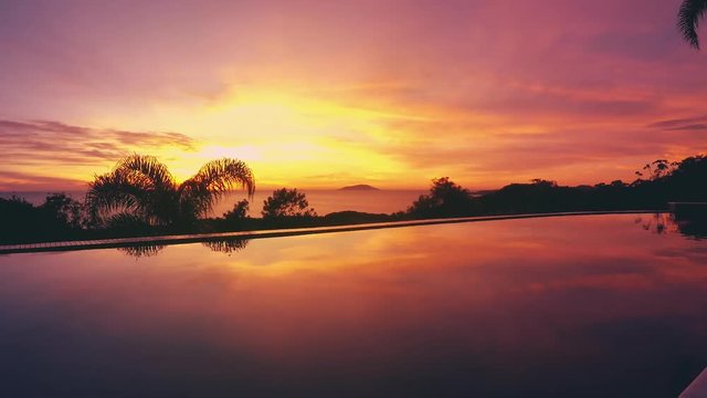 Sun rise reflected on a pool, edge of a hill with a view to the sea. Speed up sun rising, with sun beams and clouds moving. Ilha do Arvoredo island on background, Bombinhas SC, Brazil. Time lapse