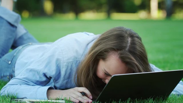 Happy woman laughing while using laptop computer on green lawn in summer park