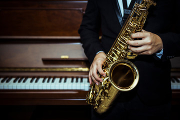 close up of Young Saxophone Player hands holding alto sax musical instrument with piano background...