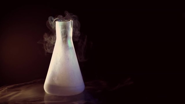 Flask with liquid nitrogen on black warm background. Concept of chemical experiments and tests. Edutainment. Copy space