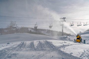 Ski lifts over snow gun and sunlit snowy mountain